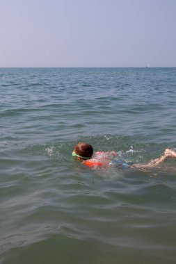 Şamandıra ve maske takan küçük bir çocuk denizde yüzüyor.