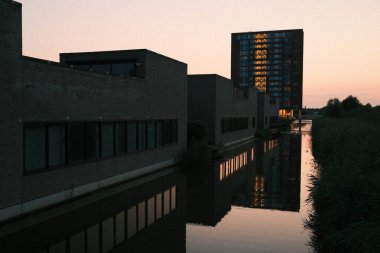 Şehir manzarasında günbatımında kanala yansıyan modern bina