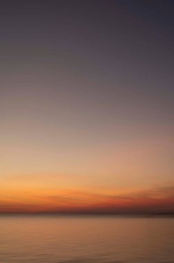 Sakin okyanus sularının üzerinde engin gökyüzü ile yumuşak bir günbatımı