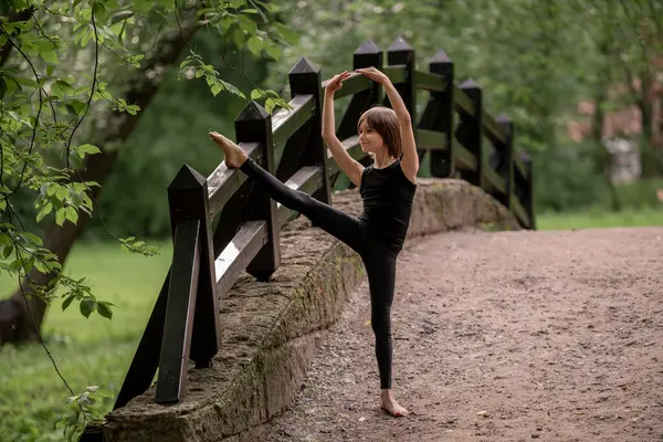 Genç bir çocuk parktaki bir köprüde bacak eklentisi yapıyor..