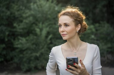 Telefonunu kullanan, gülümseyen ve mesajlaşan bir kadın..