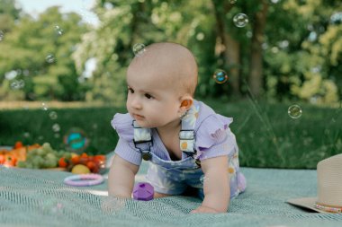 Bebek kız baloncuklarla piknik battaniyesinde oynuyor.