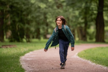 Yeşil parkta koşan kaygısız, gülümseyen çocuk.