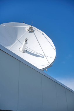 Büyük uydu anteni çatıdaki mavi gökyüzünün altında iletişim kuruyor.