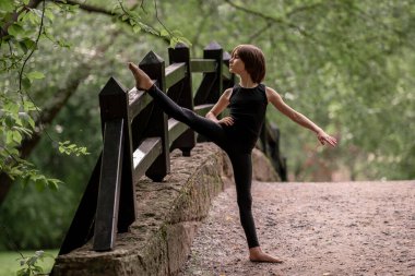 Genç bir çocuk parktaki bir köprüde bacak eklentisi yapıyor..