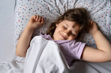 Çocuk kız büyük bir gülümsemeyle yatakta geriniyor..