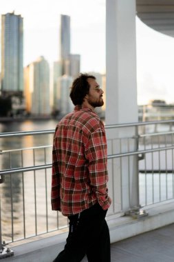 Ekose gömlek ve güneş gözlüğü takmış bir adam şehir köprüsünde yürüyor.