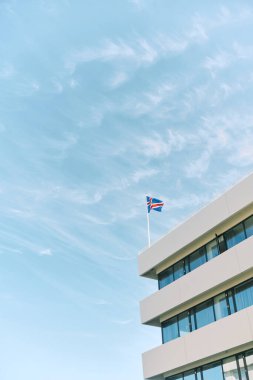 İzlanda bayrağı mavi gökyüzünün altındaki modern binaya dalgalanıyor