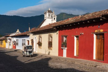 Tuc tuc taksisi boş bir sokakta kırmızı bir evin yanında gidiyor.