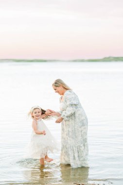 Anne ve kızı gün batımında kumsalda hassas bir anı paylaşıyorlar.