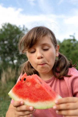 Genç kız açık havada bir dilim kırmızı karpuz yiyor..