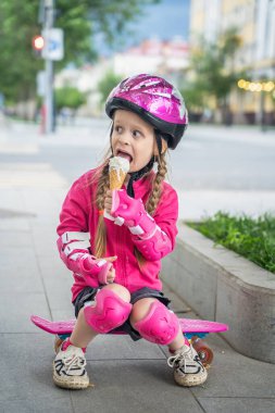 Kasklı küçük kaykaycı şehirde dondurmanın tadını çıkarıyor..