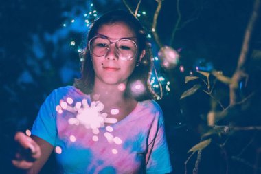 Geceleri dışarıda havai fişek tutan genç bir kadın.