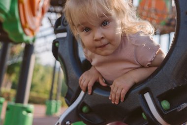 Kız dairesel bir delikten bakıyor, dışarıda eğleniyor.