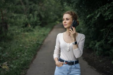 Kadın parkta yürürken telefonla konuşuyor, başka tarafa bakıyor..
