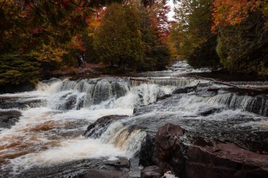 Sonbahar ağaçları ve yürüyüşçülerle dolu çok katmanlı bir şelale..