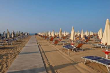 Boş güneş şezlongları ve şemsiyeler sabahın erken saatlerinde sakin bir sahilde.