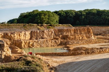 Ağaçlarla çevrili su havuzlu geniş bir taş ocağı manzarası..