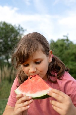 Genç kız dışarıda sulu bir karpuzu ısırıyor..