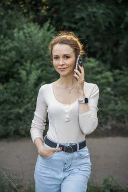 Kadın parkta yürürken telefonla konuşuyor, başka tarafa bakıyor..