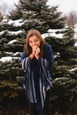 Kışın elleri ısıtan genç bir kadın. Karla kaplı çam ağaçları.