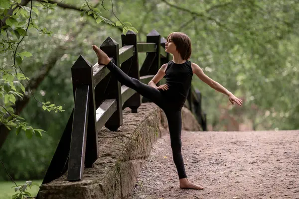 Genç bir çocuk parktaki bir köprüde bacak eklentisi yapıyor..