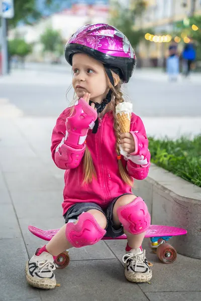 Kasklı küçük kaykaycı şehirde dondurmanın tadını çıkarıyor..