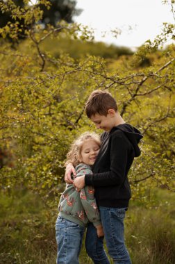 Kardeşler sonbahar ormanında sarılıp gülüyor..
