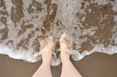 Kumsaldaki köpüklü suda çıplak ayakla tepeden aşağı bir manzara..