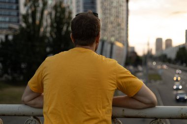 Bir adam düşünmek için durur, aşağıdaki yola bakar..