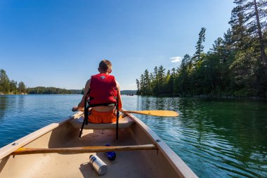 Genç bir çocuk gölde kürek çekerken bir kanonun arkasında oturuyor.
