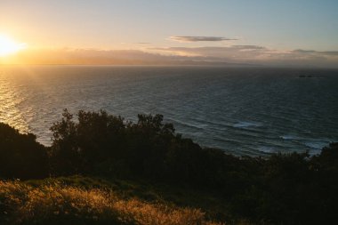 Golden Byron Körfezi günbatımı okyanus ve siluetli kıyı şeridi üzerinde.