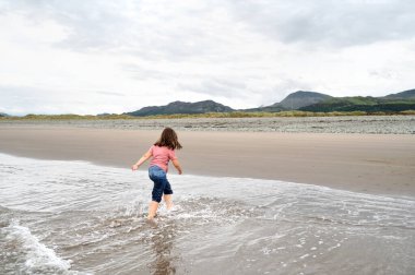 Çocuk kız arka planda dağlarla denize gidiyor..