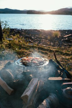Hotagen gölündeki kamp ateşinde portatif ızgarada yemek pişirmek.,