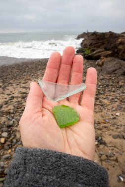 Yeşil ve akuamarin deniz camı tutan kadın eli, kayalık kıyı şeridi.