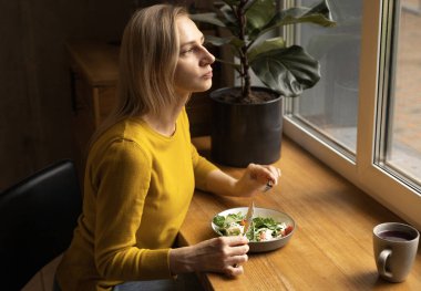 Genç bir kadın sakin bir atmosferde salatasını tadıyor.