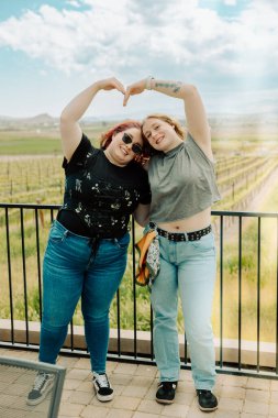 İki arkadaş, üzüm bağında kollarıyla kalp şekli oluşturur.