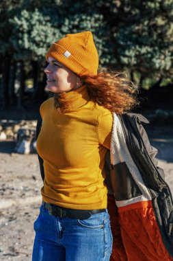 Neşeli genç bir kadın güneşli bir günde ceketini çıkarıyor.