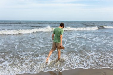 Okyanusta kumların üzerinde yürüyen bir adam aşağıya bakıyor.