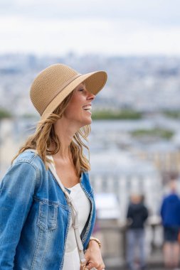 Şehre tepeden bakan şapkalı gülümseyen kadın..