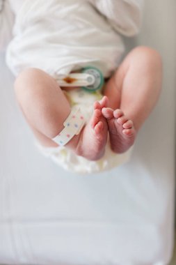 Hastane bandı ve bebek bezi takılı yeni doğmuş bebek ayaklarının yakın çekimi.