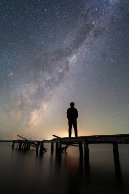 Samanyolu, gece gökyüzüne karşı duran insan siluetinin üzerinde.