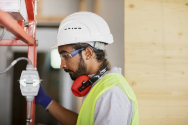 Miğferli ve ceketli işçi ahşap bir salonda çalışıyor.