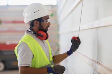 Miğferli ve ceketli işçi ahşap bir salonda çalışıyor.