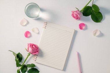 Pembe güller ve bir defter içeren güzel bir düzenleme.