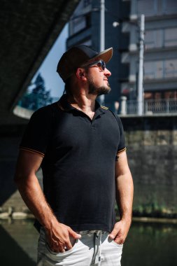 Şehirde şapka ve güneş gözlüğü takan sakallı bir adam.