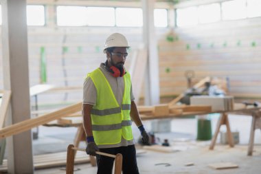 Miğferli ve ceketli işçi ahşap bir salonda çalışıyor.