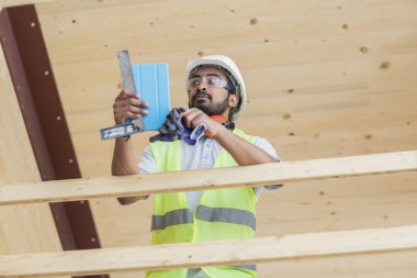 Miğferli ve ceketli işçi ahşap bir salonda çalışıyor.