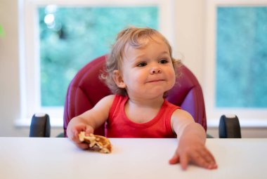 Bebek masada oturur ve elinde bir yemek tutar.