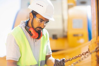 Miğferli ve ceketli işçi ahşap bir salonda çalışıyor.